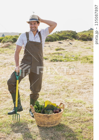 Man standing behind wicker basket holding pitchfork in dry field harvesting seasonal vegetables 135087897