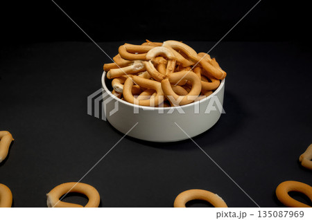 Crispy small breadsticks served on a white glass plate against a black background. Minimalistic food composition highlighting texture, contrast, and simple snack presentation. 135087969