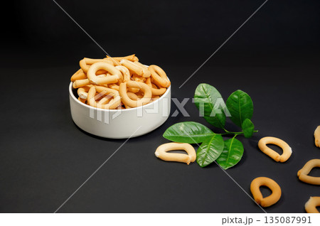 Crispy small breadsticks served on a white glass plate against a black background. Minimalistic food composition highlighting texture, contrast, and simple snack presentation. Crispy small breadsticks served on a white glass plate against a black background. Minimalistic food composition highlighting texture, contrast, and simple snack presentation. 135087991
