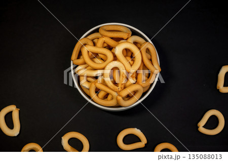 Crispy small breadsticks served on a white glass plate against a black background. Minimalistic food composition highlighting texture, contrast, and simple snack presentation. 135088013