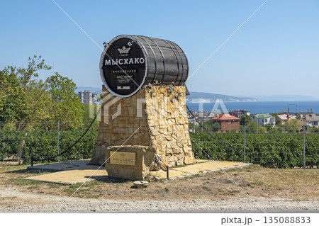August 24, 2025: Genre sculpture of a barrel with winery sign in Myskhako, Russia, with the sea and mountains on the horizon, symbolizing local winemaking, tourism and coastal landscape August 24, 2025: Genre sculpture of a barrel with winery sign in Myskhako, Russia, with the sea and mountains on the horizon, symbolizing local winemaking, tourism and coastal landscape 135088833