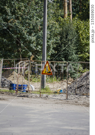 Workers are setting up a construction site surrounded by a fence. A warning sign is visible near trees and equipment scattered around the area Workers are setting up a construction site surrounded by a fence. A warning sign is visible near trees and equipment scattered around the area 135089030