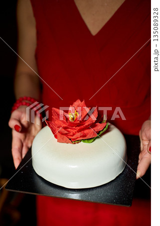 A Person Holding a Beautifully Decorated Cake Adorned With a Vibrant Flower in a Dimly Lit Setting During a Special Celebration 135089328