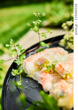 Fresh spring rolls served on a decorative tray surrounded by greenery in a vibrant outdoor setting 135089339