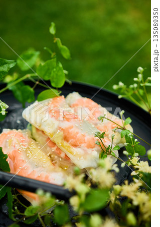Fresh spring rolls served on a decorative tray surrounded by greenery in a vibrant outdoor setting 135089350