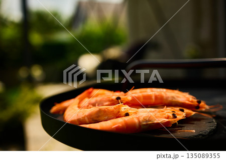 Grilled shrimp on a black grill plate surrounded by green grass in a sunny outdoor setting Grilled shrimp on a black grill plate surrounded by green grass in a sunny outdoor setting 135089355