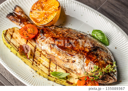 grilled whole dorado fish with vegetables and lemon on a white plate. top view 135089367