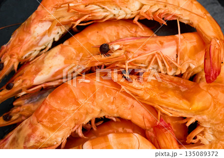 Grilled shrimp on a black grill plate surrounded by green grass in a sunny outdoor setting 135089372