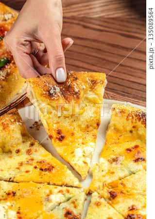Hand holding a slice of cheesy Italian pizza with golden crust on a wooden table. copy space 135089564