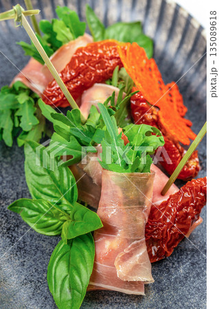 Prosciutto rolls with arugula and sun-dried tomatoes on a dark plate. top view Prosciutto rolls with arugula and sun-dried tomatoes on a dark plate. top view 135089618