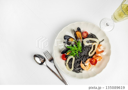 Black spaghetti with seafood and arugula on a white plate. top view. copy space Black spaghetti with seafood and arugula on a white plate. top view. copy space 135089619
