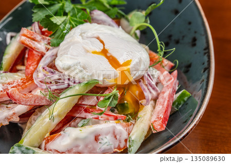 Fresh vegetable salad with creamy dressing topped by a perfectly poached egg with runny yolk on a ceramic plate Fresh vegetable salad with creamy dressing topped by a perfectly poached egg with runny yolk on a ceramic plate 135089630