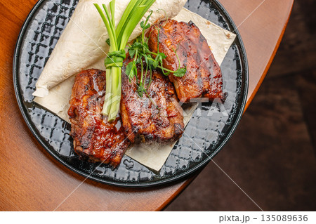 Barbecue pork ribs served with flatbread and green onion garnish on a black ceramic plate 135089636