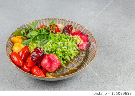 Assorted pickled vegetables including cucumbers, peppers, cabbage, onions, and fresh lettuce garnished with parsley in a rustic bowl Assorted pickled vegetables including cucumbers, peppers, cabbage, onions, and fresh lettuce garnished with parsley in a rustic bowl 135089658