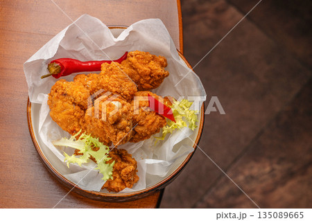 Crispy golden fried chicken pieces served in a bowl with chili pepper and fresh lettuce on parchment paper Crispy golden fried chicken pieces served in a bowl with chili pepper and fresh lettuce on parchment paper 135089665