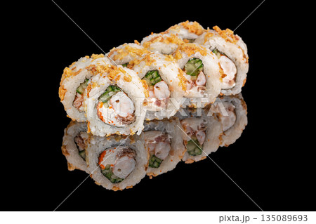 Sushi rolls filled with shrimp, cream cheese, cucumber, and crunchy toppings are neatly arranged and reflected on a glossy black surface 135089693