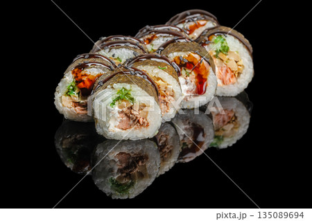 Sushi rolls filled with salmon, cream cheese, greens, and vegetables are topped with dark sauce and elegantly displayed on a black reflective surface Sushi rolls filled with salmon, cream cheese, greens, and vegetables are topped with dark sauce and elegantly displayed on a black reflective surface 135089694