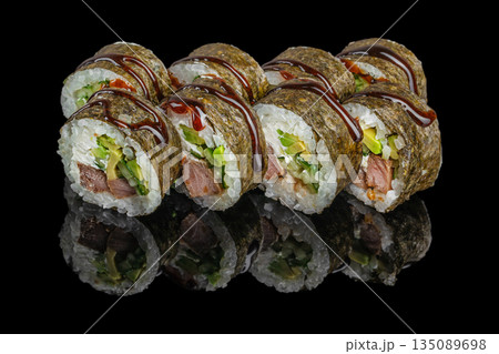 Sushi rolls wrapped in nori and filled with rice, avocado, cucumber, cream cheese, and cooked meat are drizzled with dark teriyaki sauce and displayed on a reflective black surface 135089698