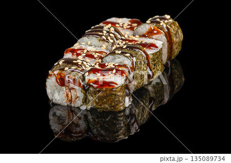 Sushi rolls wrapped in nori are generously drizzled with glossy teriyaki sauce and sprinkled with sesame seeds, beautifully reflected on a sleek black surface 135089734