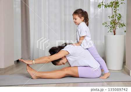Mother and daughter bonding during a playful yoga session on a mat Mother and daughter bonding during a playful yoga session on a mat 135089742