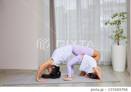 Mother and daughter exercising in a bridge pose on a mat at home Mother and daughter exercising in a bridge pose on a mat at home 135089766