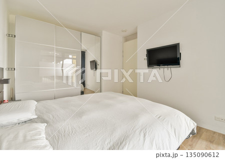 A spacious and bright modern bedroom featuring a minimal design with a neatly made bed and wall-mounted TV, perfect for relaxation and comfort. A spacious and bright modern bedroom featuring a minimal design with a neatly made bed and wall-mounted TV, perfect for relaxation and comfort. 135090612