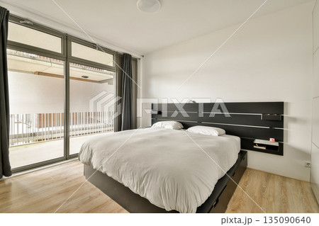 A sleek and stylish modern bedroom featuring neutral tones, a comfortable bed, and large windows that invite natural light, creating a serene atmosphere. A sleek and stylish modern bedroom featuring neutral tones, a comfortable bed, and large windows that invite natural light, creating a serene atmosphere. 135090640