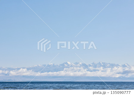 Calm blue ocean with distant snow-capped mountain range under clear sky Calm blue ocean with distant snow-capped mountain range under clear sky 135090777