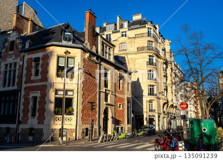 Residential architecture stands in Paris, France. Street corner in the 17th district features a historic brick mansion and classic stone buildings with public bicycles Residential architecture stands in Paris, France. Street corner in the 17th district features a historic brick mansion and classic stone buildings with public bicycles 135091239