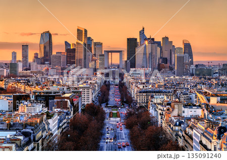 La Defense business district skyline stands near Paris, France. Sunset view from Arc de Triomphe features Avenue de la Grande Armee and modern skyscrapers under an orange sky 135091240