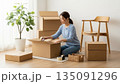 明るい白い部屋で段ボールを開ける新生活の女性 135091296
