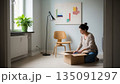 明るい白い部屋で段ボールを開ける新生活の女性 135091297