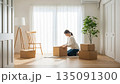 明るい白い部屋で段ボールを開ける新生活の女性 135091300