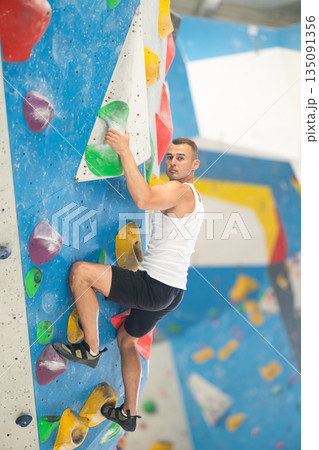 Atlete man grabbing ledges of artificial climbing wall in bouldering centre Atlete man grabbing ledges of artificial climbing wall in bouldering centre 135091356