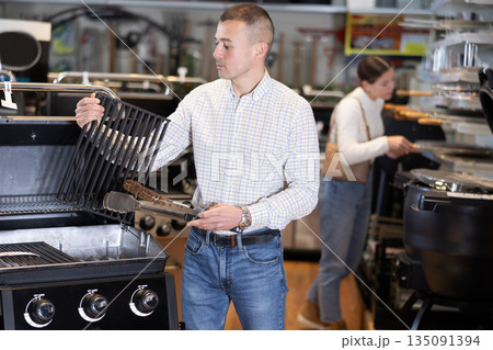 In store, man inspects mobile grill, buys barbecue device In store, man inspects mobile grill, buys barbecue device 135091394