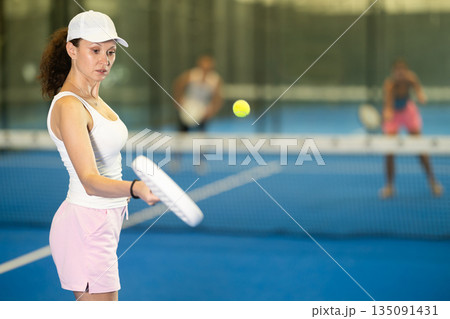 Woman playing padel on indoor court on summer day. Sport and active lifestyle concept Woman playing padel on indoor court on summer day. Sport and active lifestyle concept 135091431