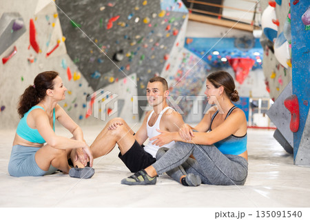 Three climbing friends sit on the floor and discuss options for climbing climbing wall. Share their impressions 135091540