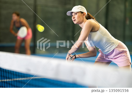 Woman playing padel on indoor court on summer day. Sport and active lifestyle concept Woman playing padel on indoor court on summer day. Sport and active lifestyle concept 135091556