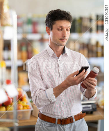 Man in light shirt scan QR code and take reading red smoothie label using phone camera in shop 135091597