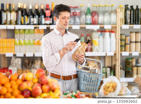 Man in light shirt scan QR code and take reading wine using phone camera in shop 135091602