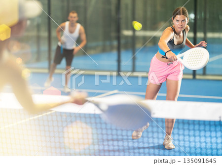 Girl paired with a man plays padel on an indoor tennis court Girl paired with a man plays padel on an indoor tennis court 135091645