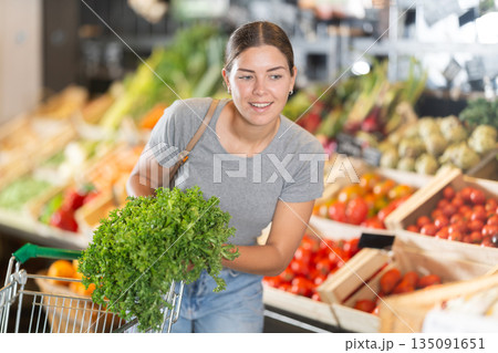Young girl purchaser buying bunch of fresh parsley in grocery store Young girl purchaser buying bunch of fresh parsley in grocery store 135091651