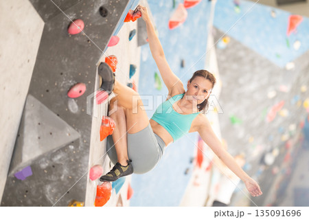 Middle-aged woman climbing on artificial rock wall in rock-climbing gym Middle-aged woman climbing on artificial rock wall in rock-climbing gym 135091696