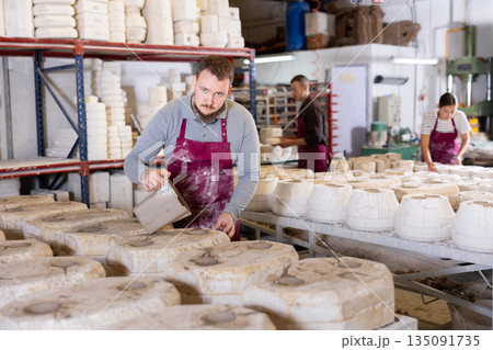 Ceramicist pouring liquid clay into slipcasting molds in pottery workshop 135091735