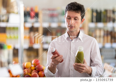 Man in light shirt choose and buy fruit smoothie in store Man in light shirt choose and buy fruit smoothie in store 135091739