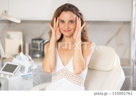 Young joyful woman examining her face after cosmetic procedure 135091761