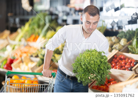 Young man purchaser buying bunch of fresh parsley in grocery store Young man purchaser buying bunch of fresh parsley in grocery store 135091762