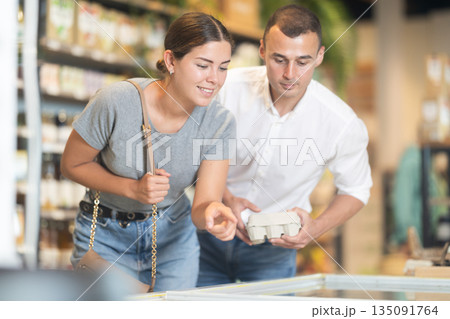 Young couple making choice leaning over shop-fridge in supermarket 135091764