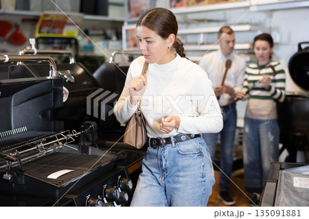 Young woman choosing BBQ grill in store Young woman choosing BBQ grill in store 135091881