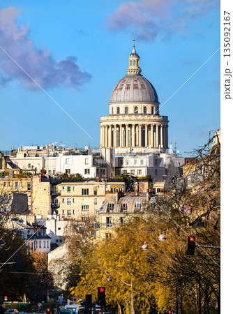 Pantheon monument stands in Paris, France. City skyline features the historic dome rising above residential buildings and zinc roofs under a blue sky 135092167